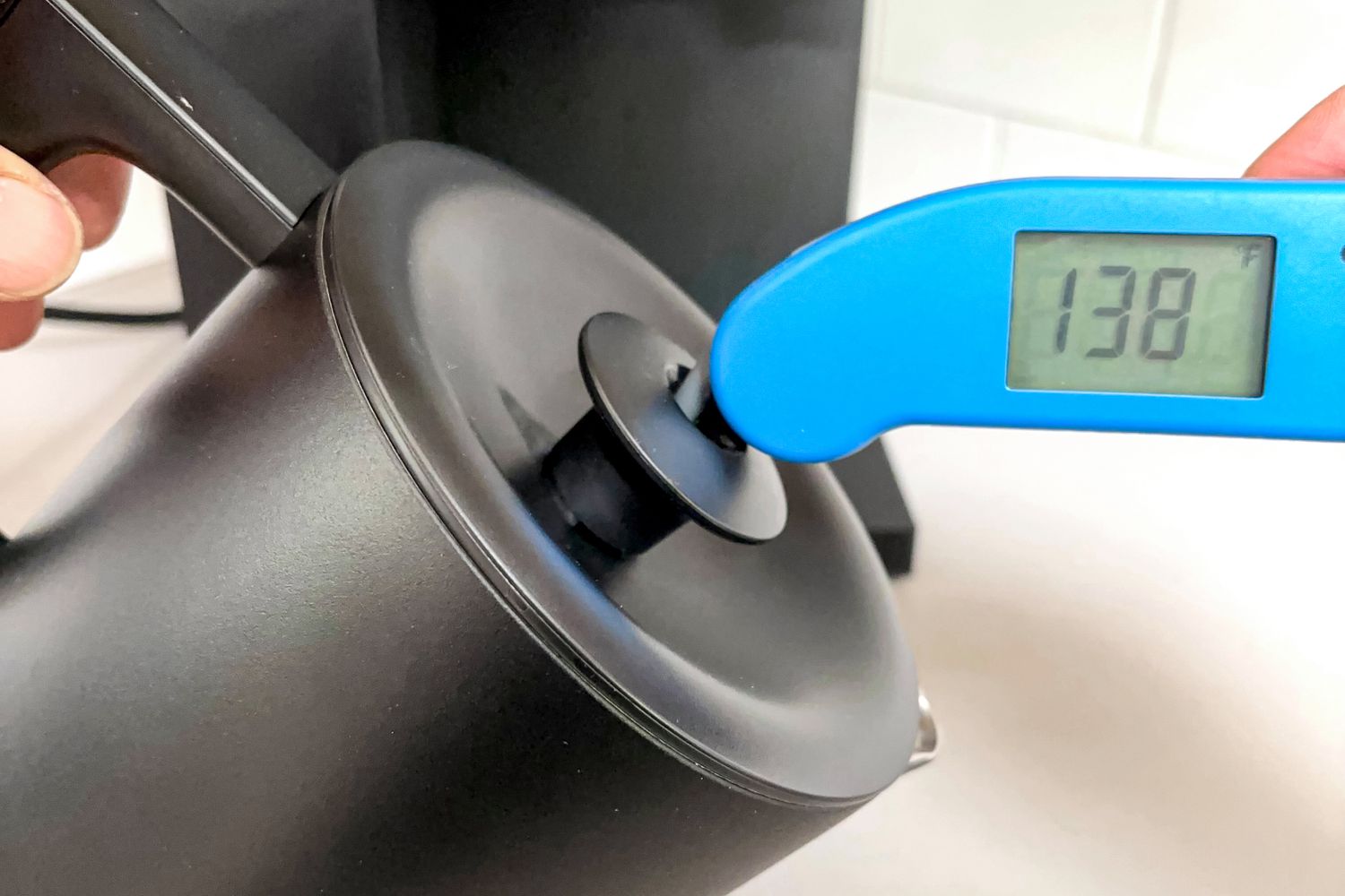 A person taking the temperature of coffee in a coffee makers carafe.