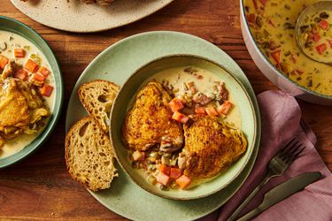 A plate of chicken served with vegetables and bread next to a bowl of soup