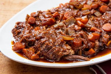 A white oval platter of Jewish-style braised brisket with onions and carrots, and jus pooling beneath the brisket.