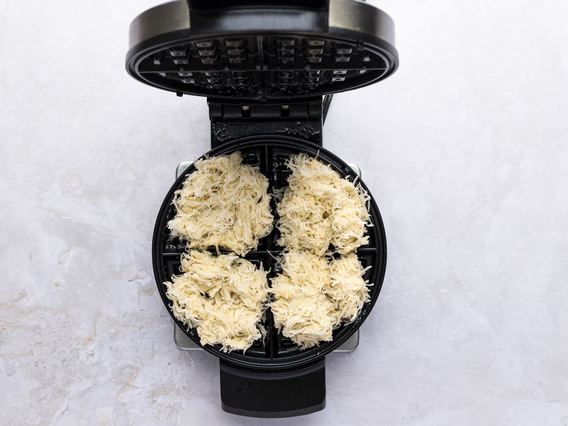 The open waffle iron with the shredded potatoes placed inside.