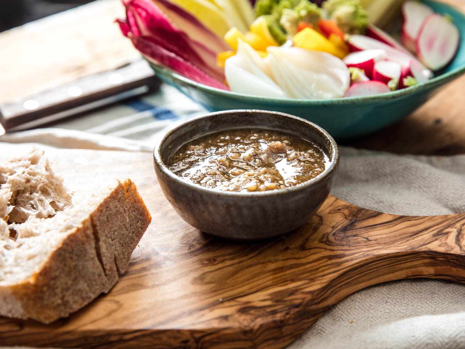 A bowl of bagna cauda served with crusty bread and raw vegetables.