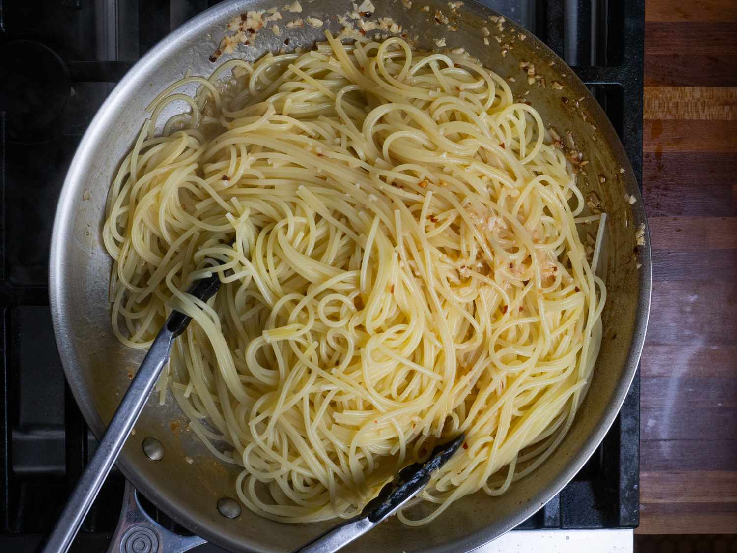 Spaghetti being tossed with tongs in the skillet with the sauce.