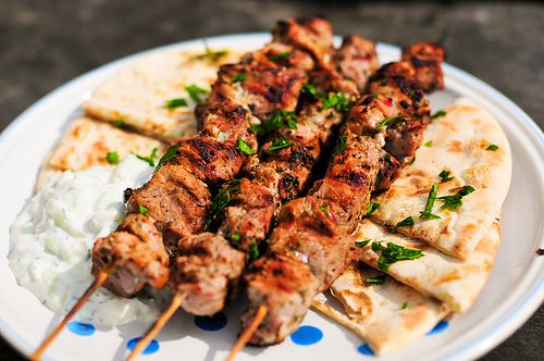 Skewers of grilled meat served with pita bread and a side of tzatziki sauce on a plate