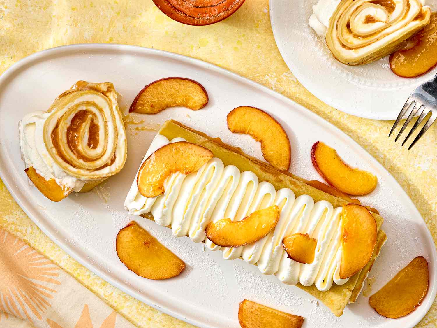 Dessert dish with peaches and cream crepe rolls served on a white platter with peach slices as garnish
