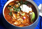 A bowl of slow-cooker chicken tortilla soup, topped with cilantro, avocado, sour cream, red onion, and lime.