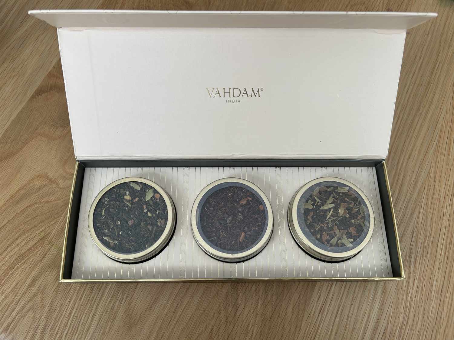 A box of three tins of looseleaf teas on a wooden surface.