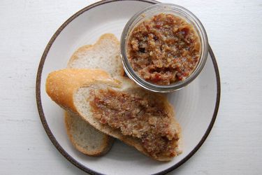 Overhead view of a canning jar of bacon-bourbon jam, served on a plae with two slices of baugette.