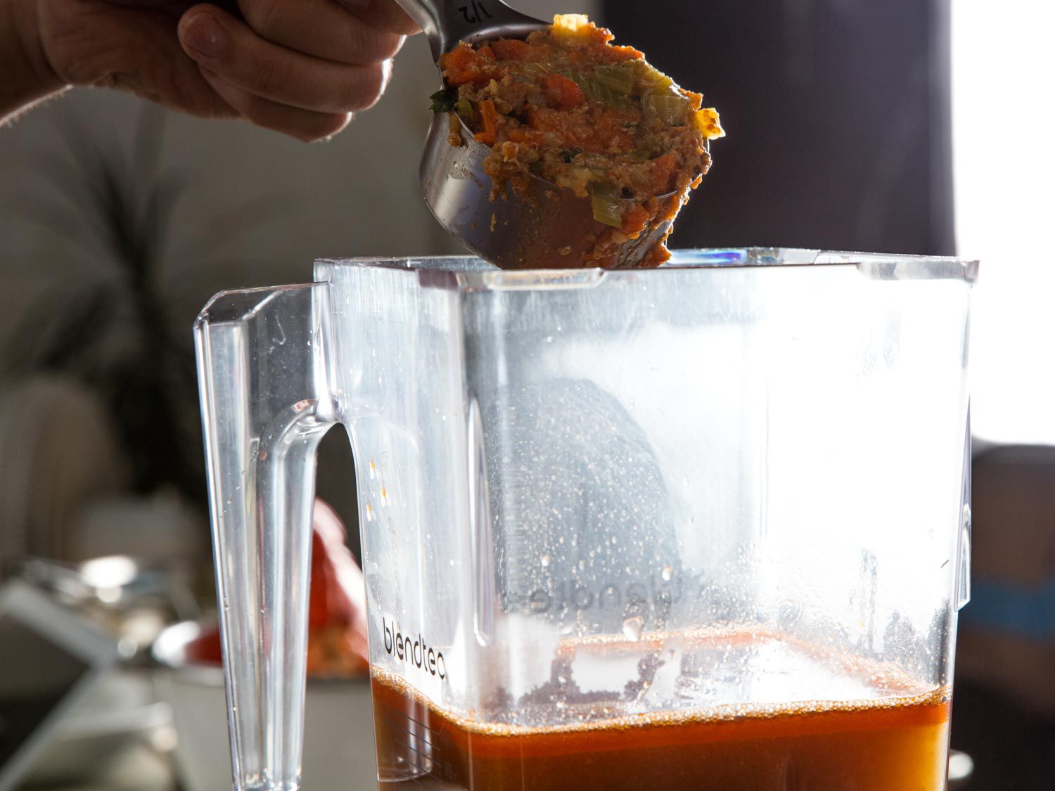 Chopped vegetables used for making the lobster stock being scooped into a blender partly filled with fat-enriched stock.