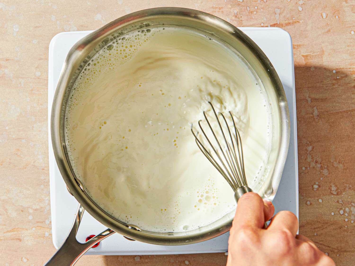 A hand whisking liquid in a saucepan on a stovetop