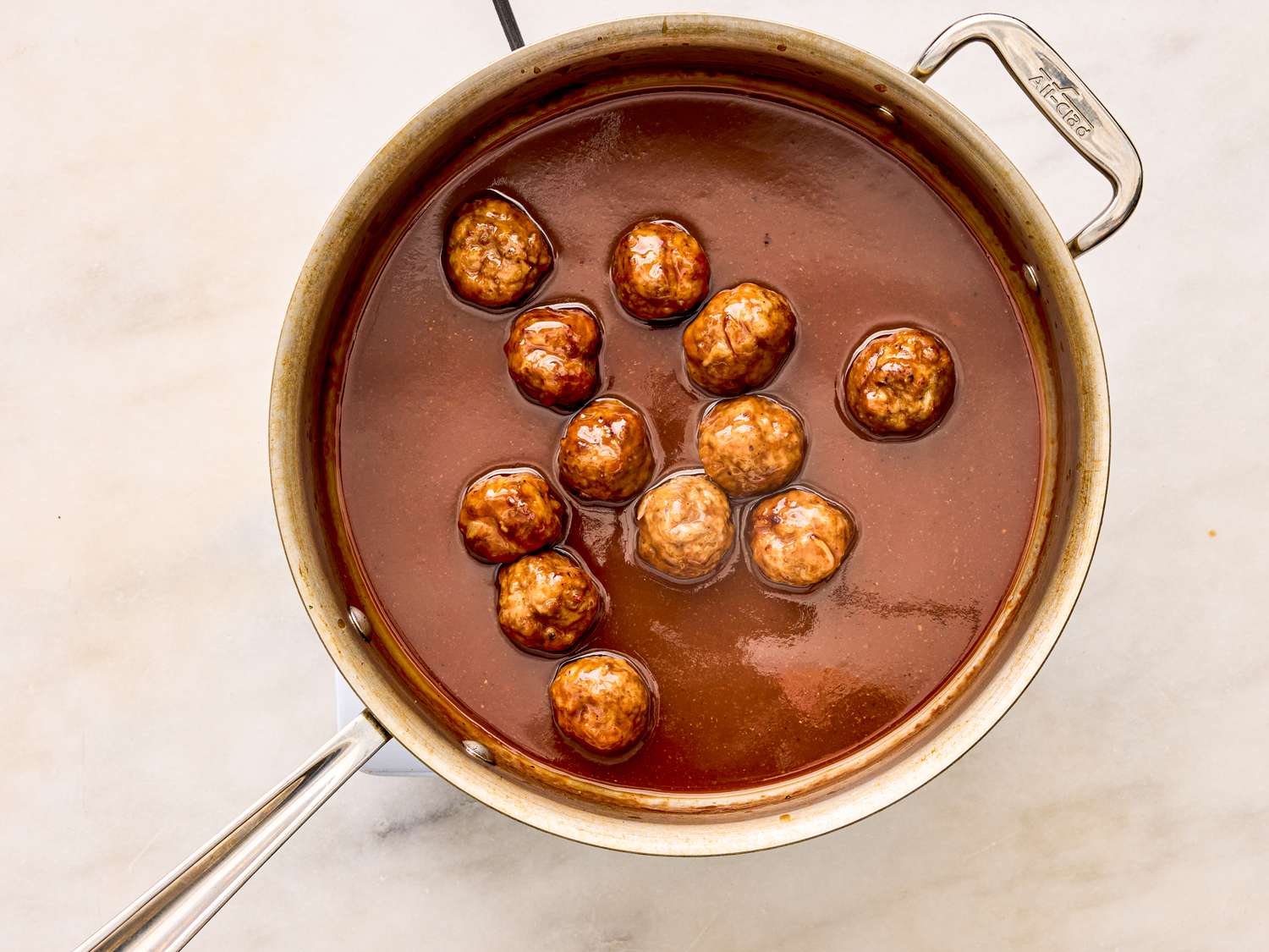 A pot containing meatballs in a red sauce on a marble surface