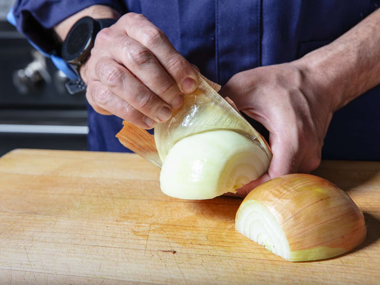 Hands peeling off outer layer of half an onion.