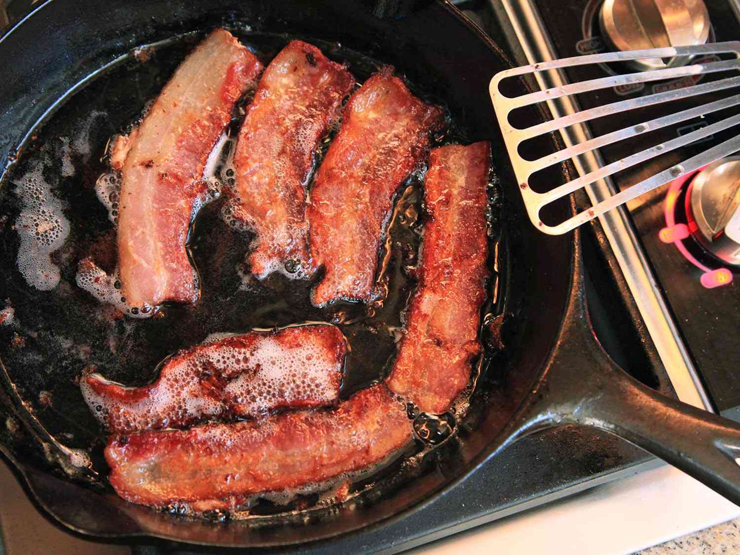 Strips of bacon frying in a cast iron skillet