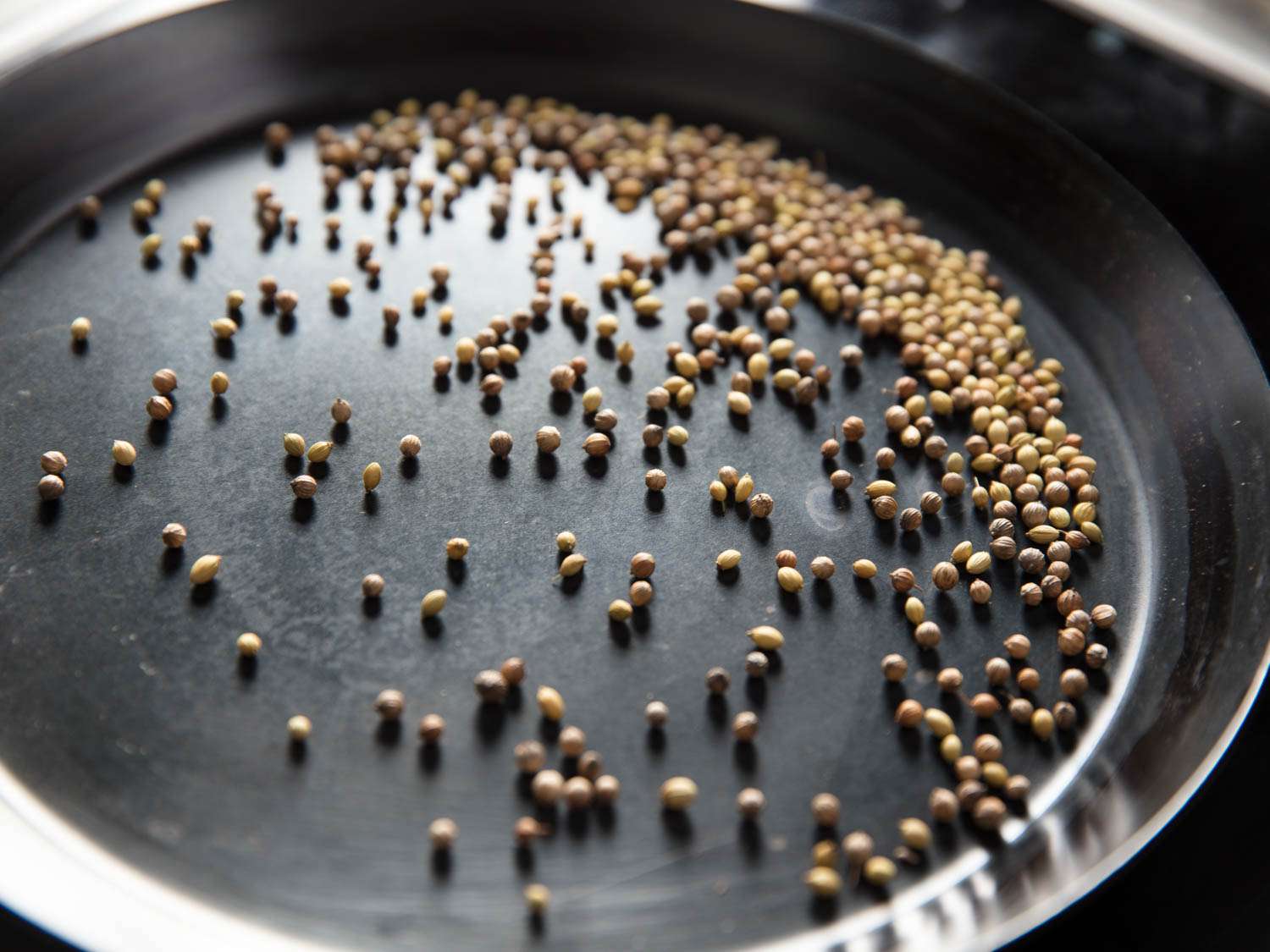Coriander seeds are toasted in a carbon steel pan.