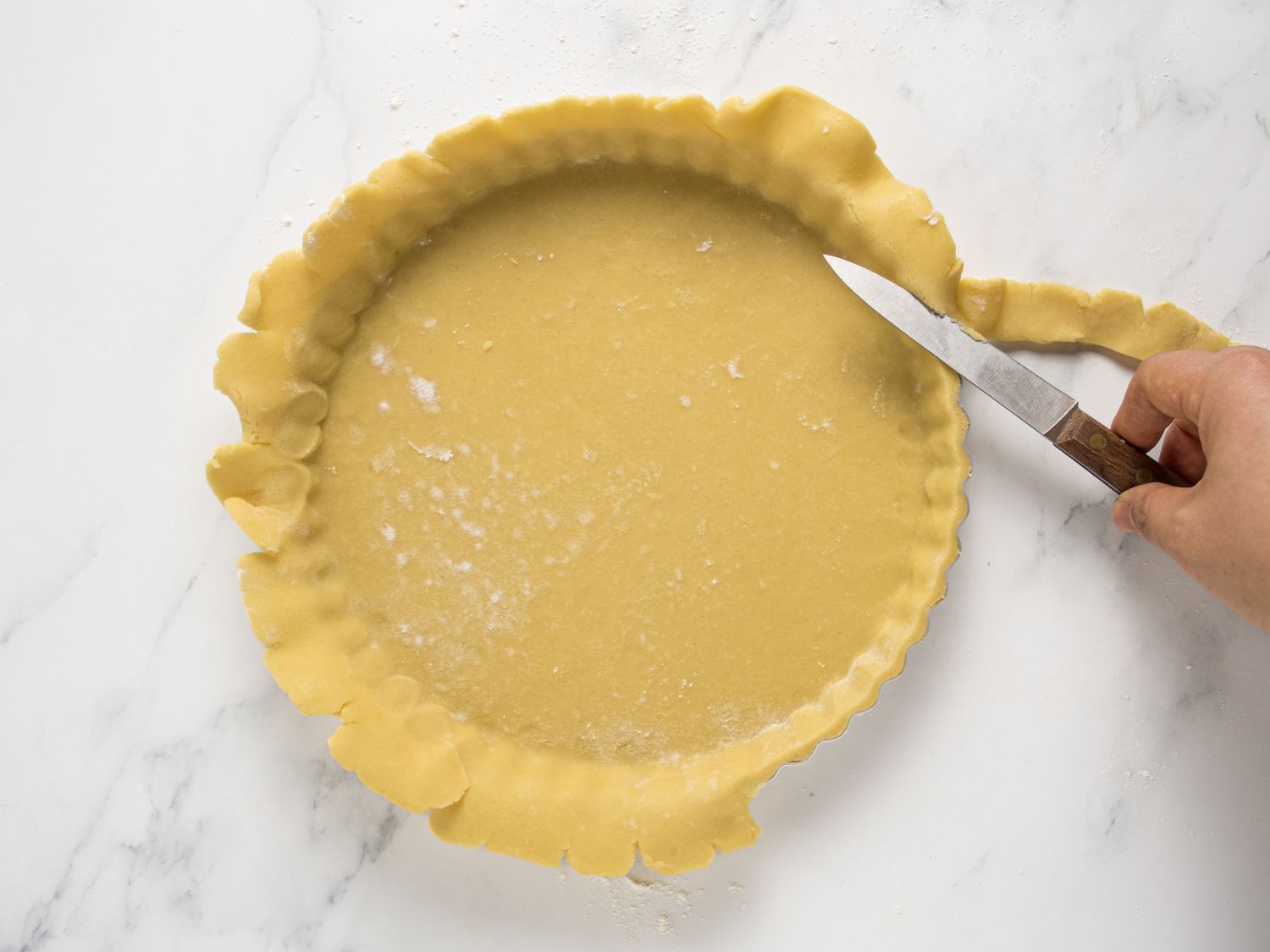 Trimming the ends f the extra uncooked crust off of pie pan with a paring knife 