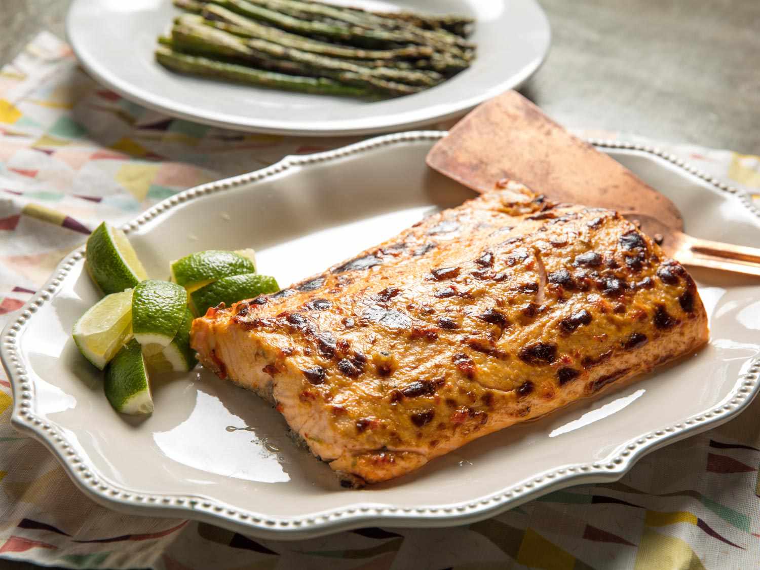 A large broiled salmon fillet with chile-lime mayo, served on a platter with lime wedges.