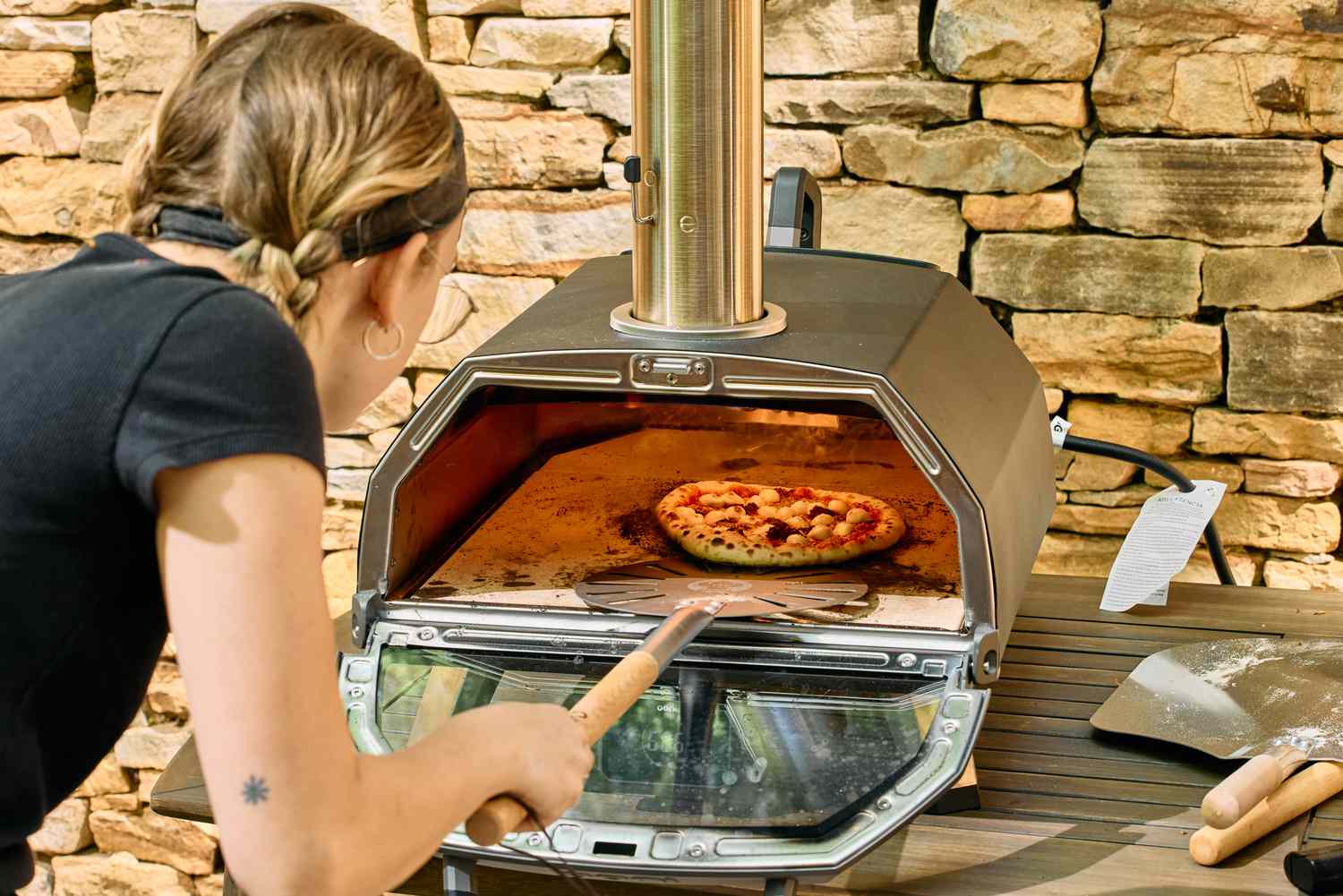 A person removes a pizza from the Ooni Karu 2 Pro Multi-Fuel Pizza Oven