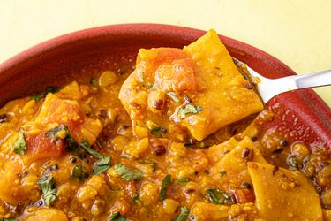 A spoonful of lentil curry with vegetables and garnished herbs being lifted from a bowl