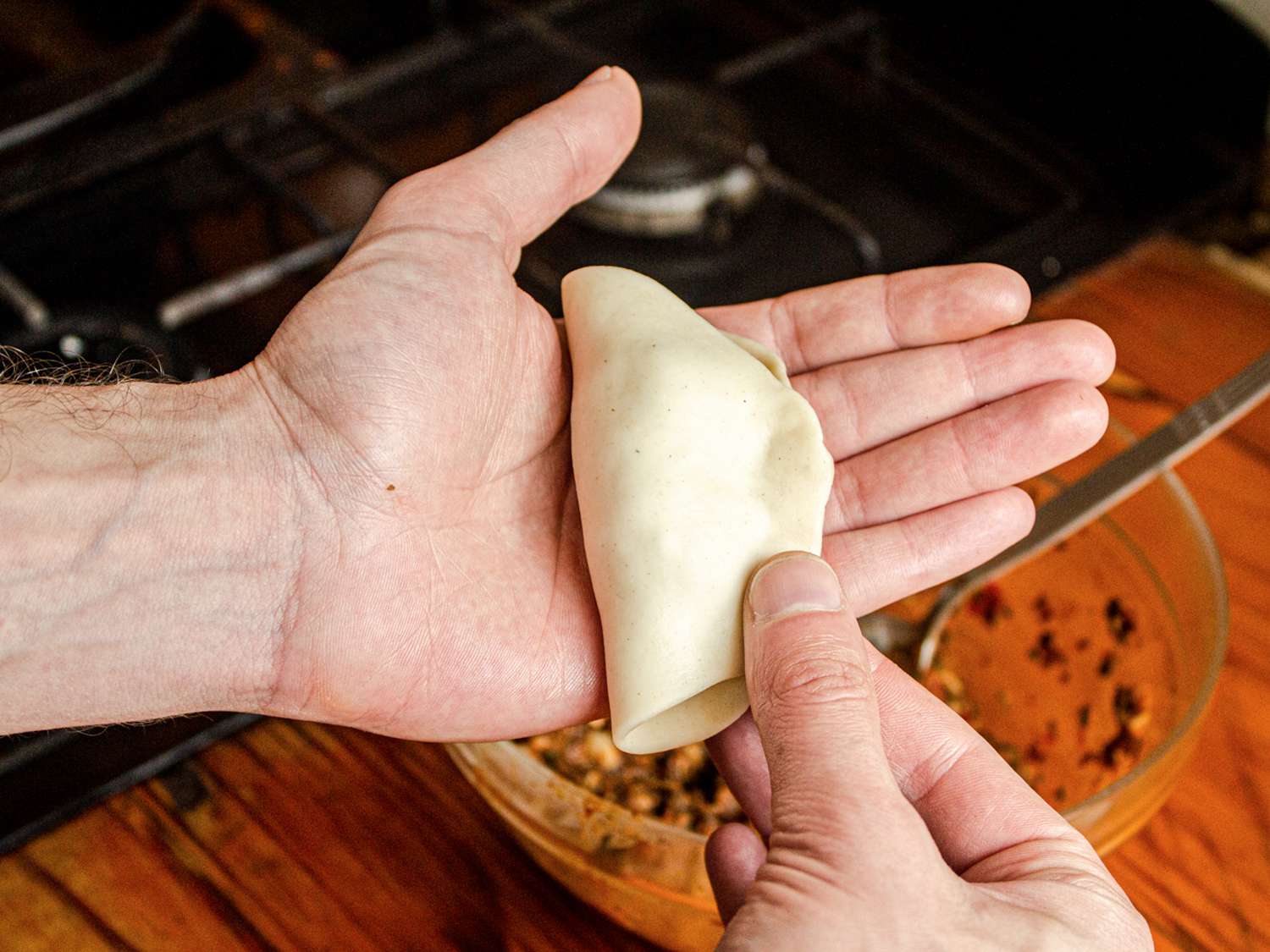 Overhead view of a hand folding a piece of dough over filling