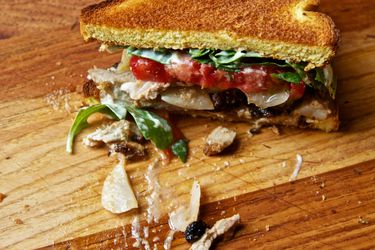 Half of a turkey club shawarma sandwich with pork belly and enhanced mayo on a cutting board. A few stray pieces of sandwich filling are strewn on the cutting board.