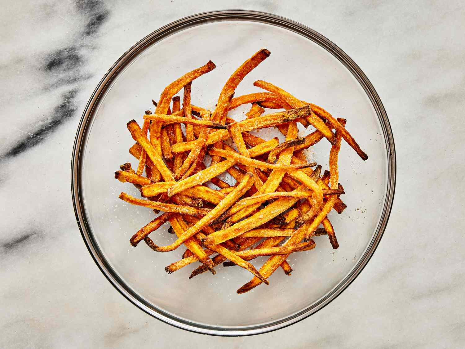 Cooked fries tossed in a glass bowl with salt