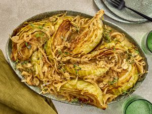 cabbage on a platter with plates, forks and green napkins, and cups on the sides