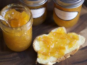 Several jars of honey tangerine marmalade. One has been opened and a piece of toast topped with the marmalade is nearby.