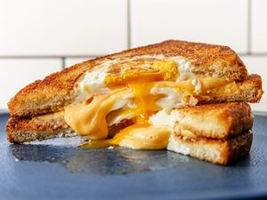 Two halves of a grilled cheese egg-in-the-hole sandwich stacked on top of each other, with cheese and egg overflowing from the middle. 