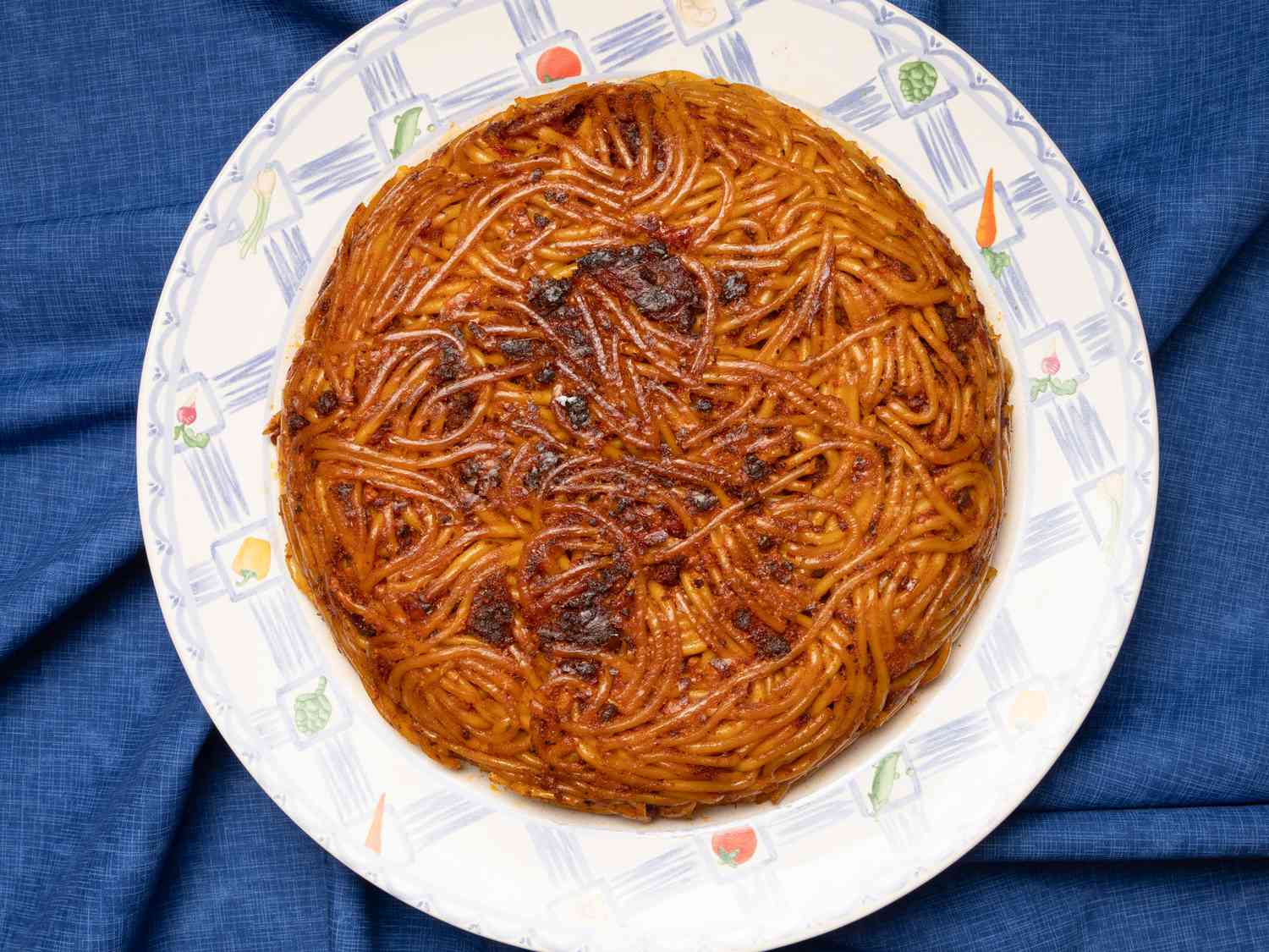 A dish of tahdig macaroni arranged on a patterned plate on a blue fabric surface