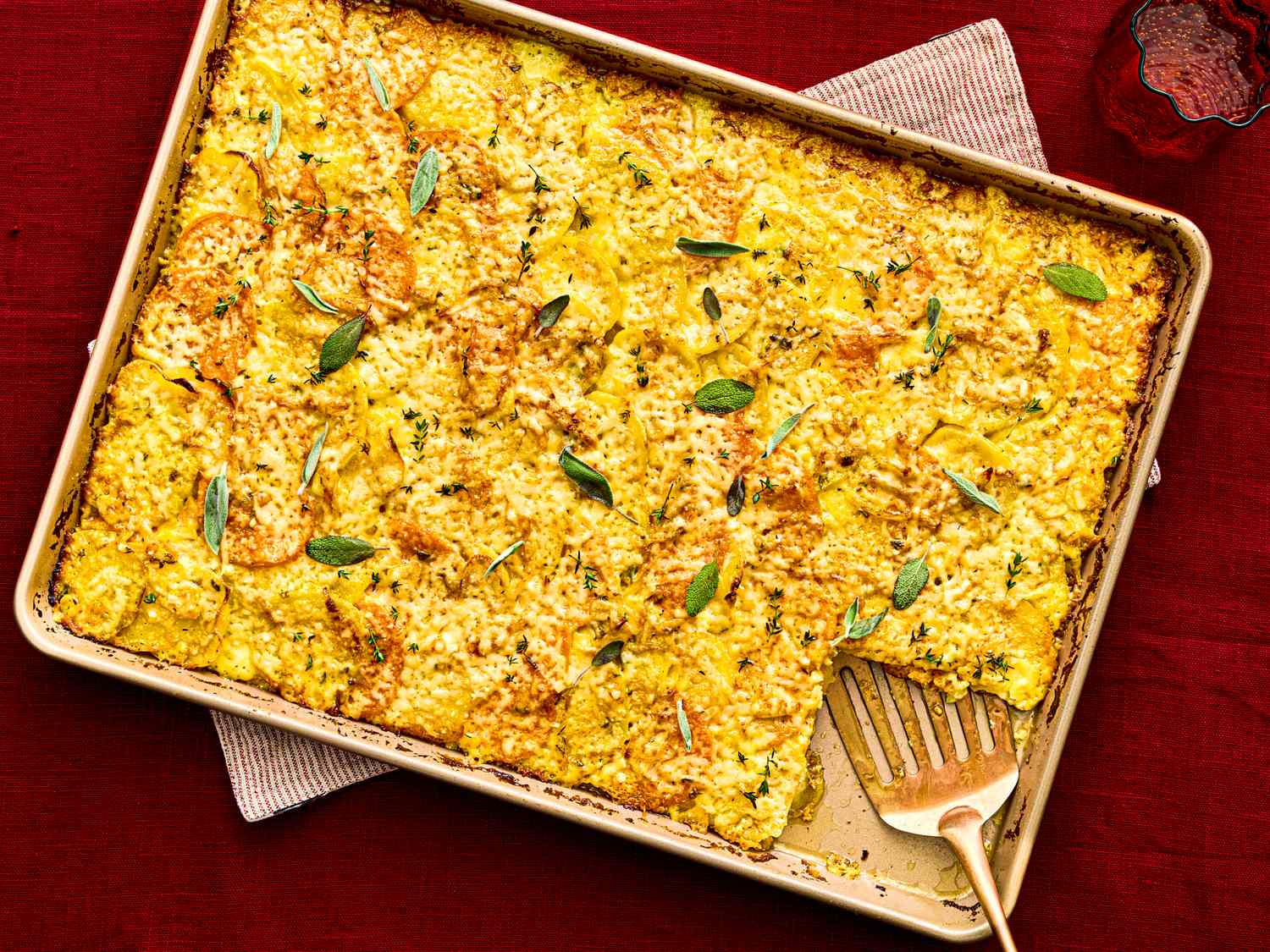 Baked root vegetable gratin in a sheet pan garnished with herbs and partially served with a fork