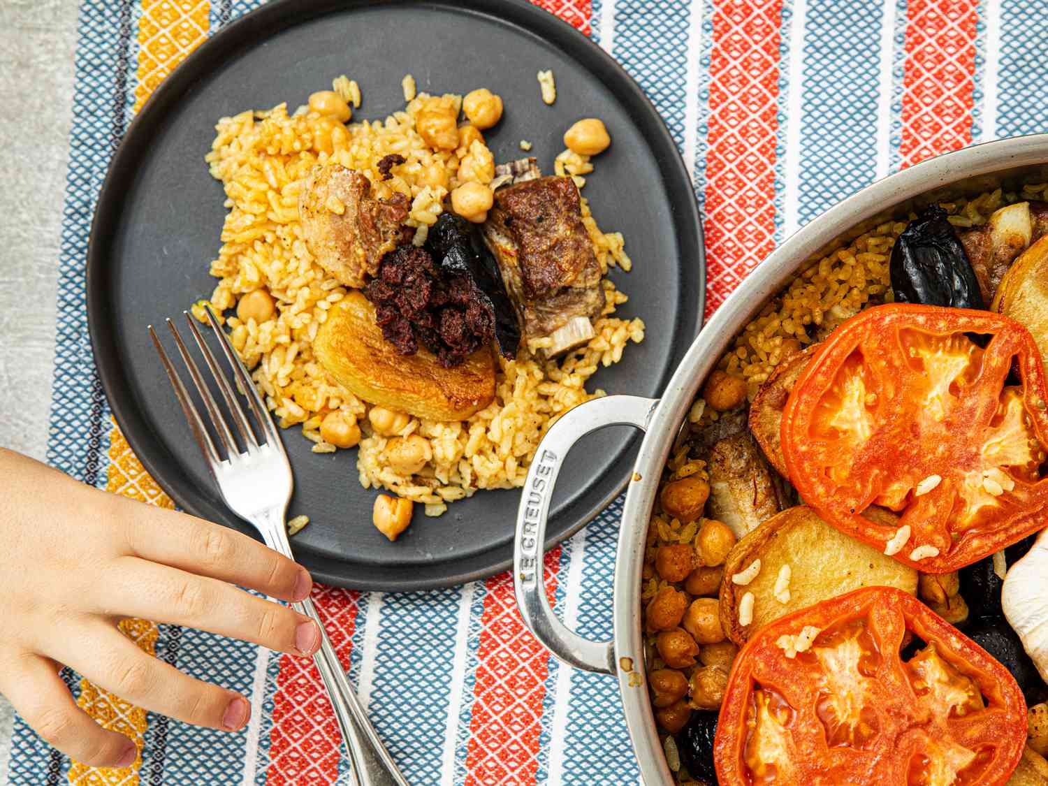 Overhead view of a serving of arroz al horno and a child's hand reaching for a fork.