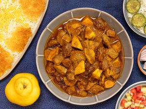 A dish of khoreshe beh alongside sides like rice and other accompaniments