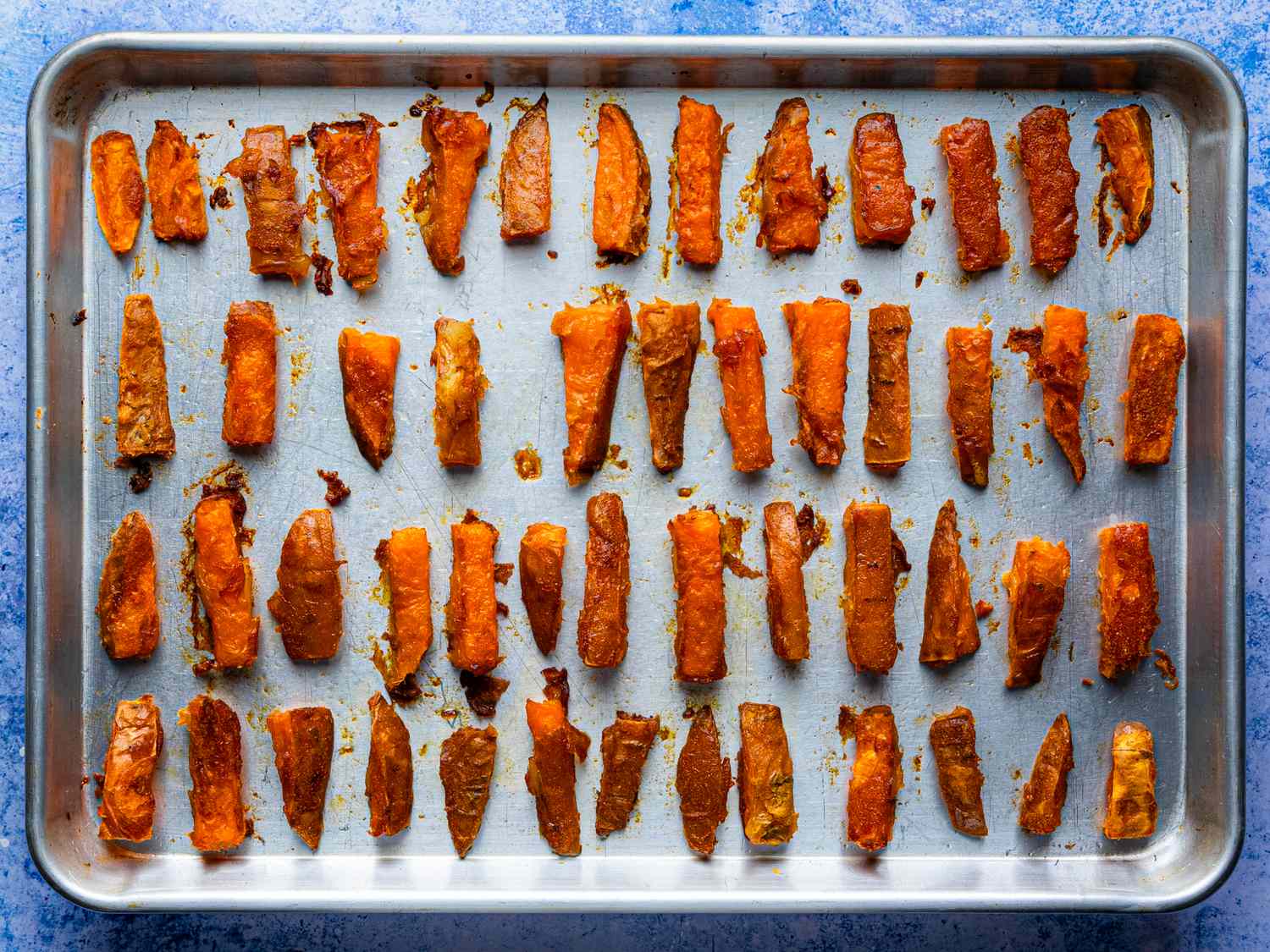 A tray of ovenbaked sweet potato fries arranged in neat rows on a metal baking sheet