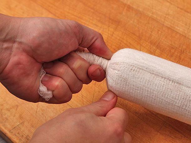 Author holding one end of the cheesecloth-wrapped foie gras with one hand and winding twine around the gathered cloth with the other.