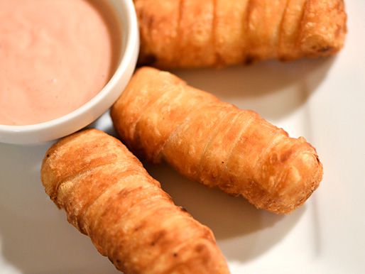 Three tequenos resting on a plate next to some dipping sauce.