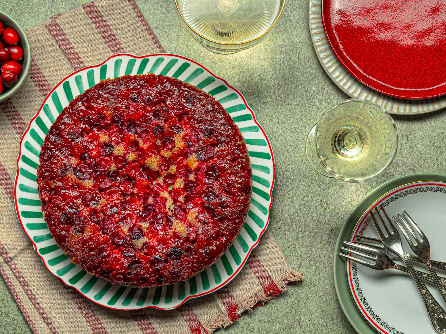 Cranberry upsidedown cake on a decorated plate with tableware and glasses of white wine nearby