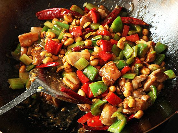 Takeout-style kung pao chicken in wok with a metal spatula.