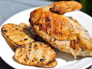 Closeup of a breast and attached wing of Cornell chicken, served with grilled potato slices.