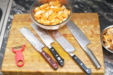 four nakiri knives on a cutting board with a bowl of cut up sweet potatoes