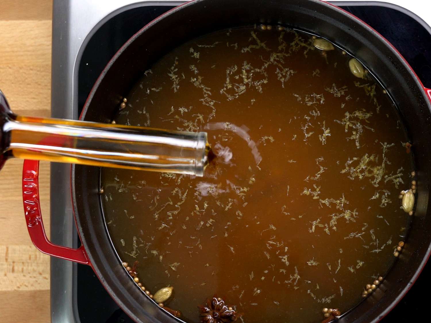 Liquor being poured from a long-necked bottle into a pot of apple cider and mulling spices