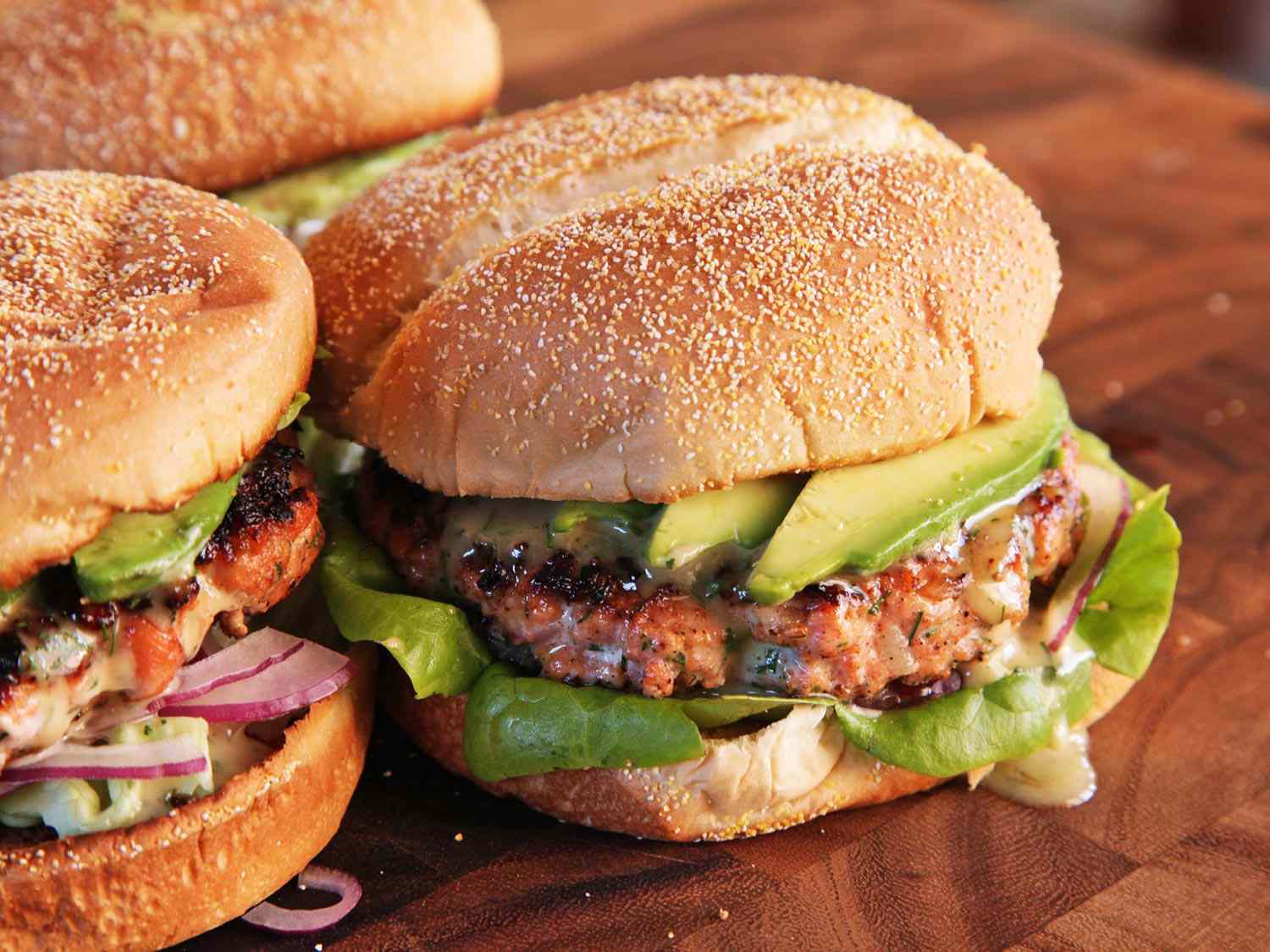 Closeup of the assembled salmon burgers on a wooden cutting board.