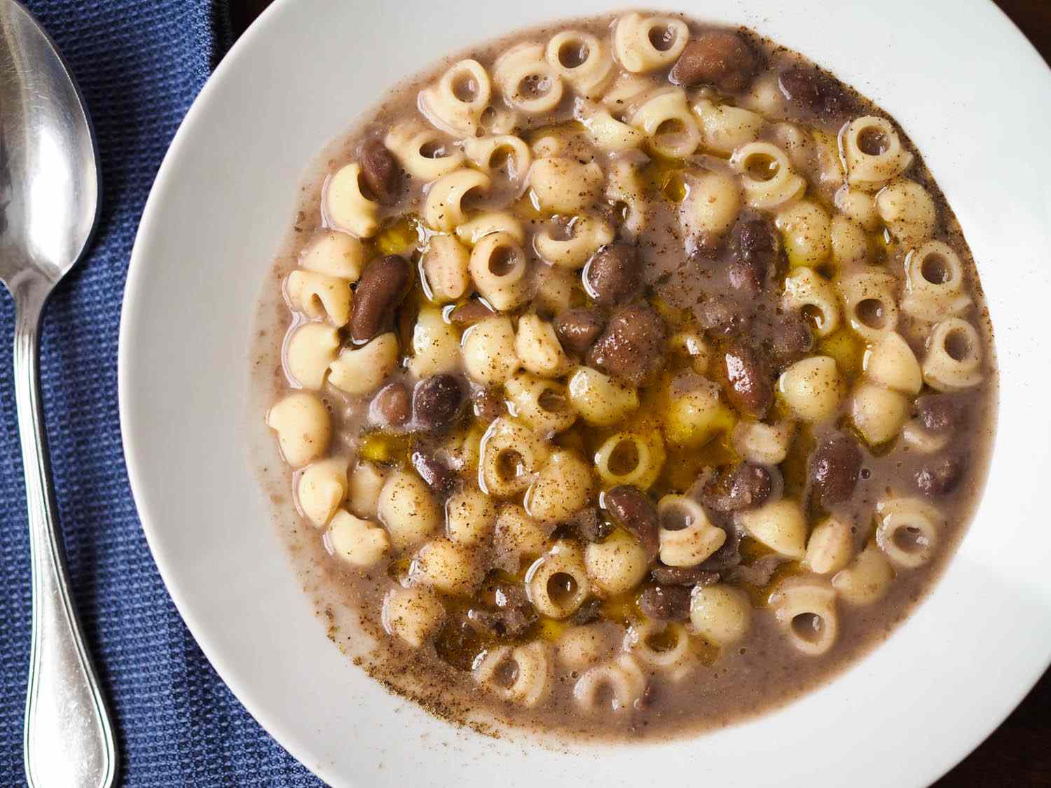 Overhead close-up of a serving of pasta e fagioli, drizzled with olive oil and seasoned with freshly ground black pepper.