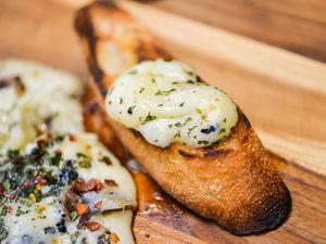 Closeup of a toasted slice of baguette topped with grilled and seasoned provoleta cheese.