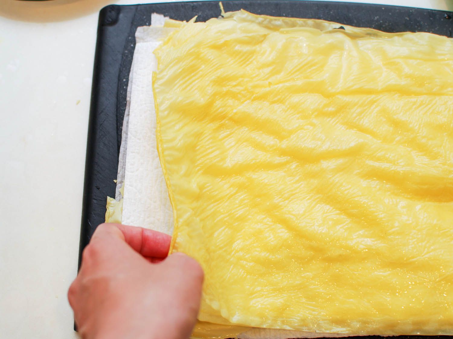 Rehydrated bean curd sheets are stacked between layers of paper towel.
