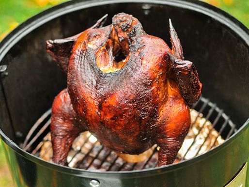 Whole smoked turkey propped vertically on a beer can in a grill