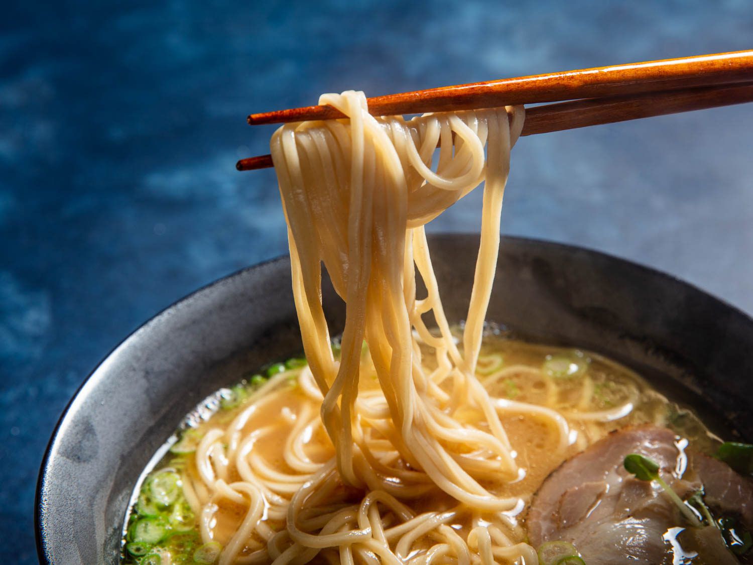 Homemade alkaline noodles being pulled out of a bowl of ramen with chopsticks