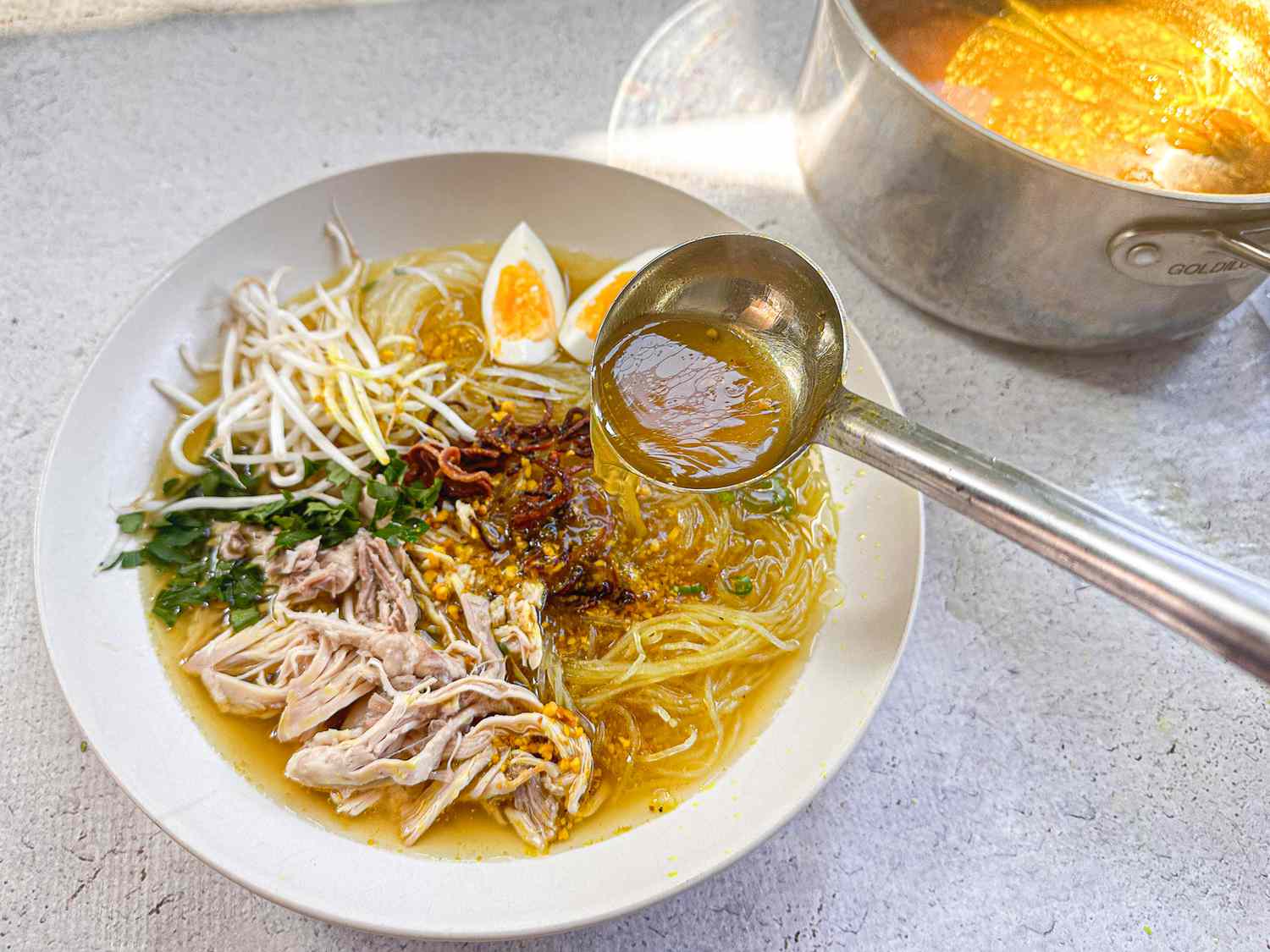 spooning broth onto soup bowl