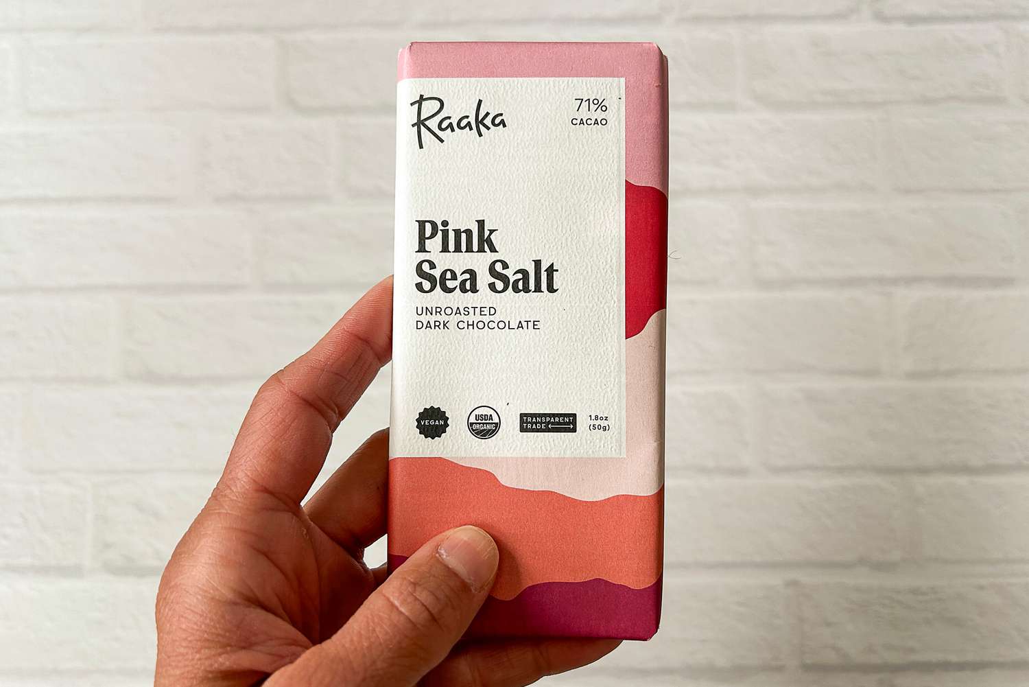 A person holding the The Raaka Pink Sea Salt Dark Chocolate Bar