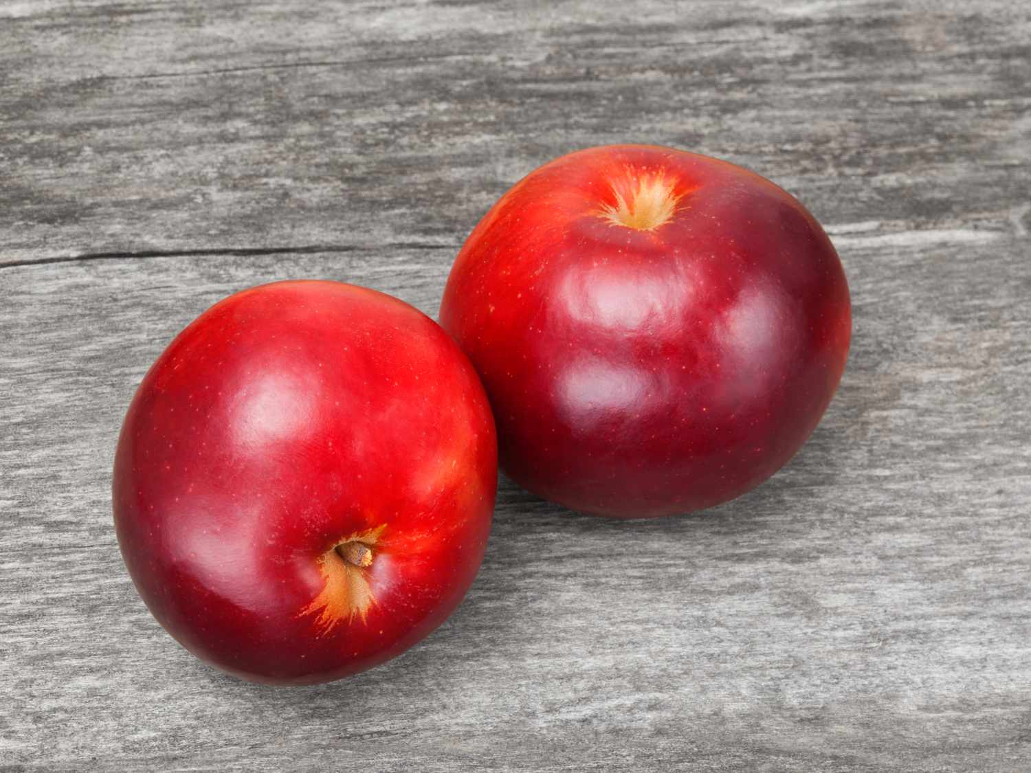 Two red apples placed on a wooden surface