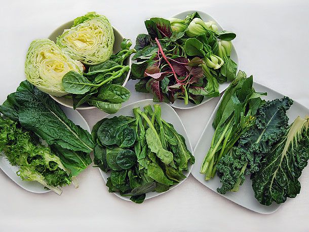 An assortment of different varieties of Chinese greens on five white plates. 