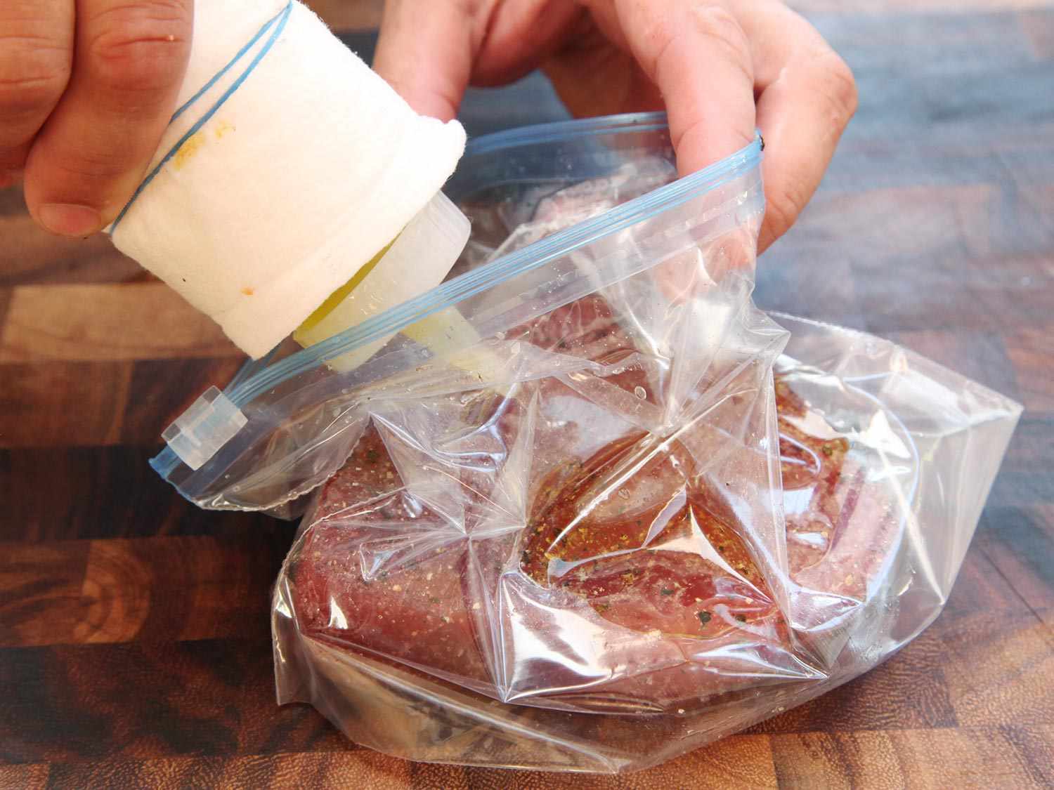 Seasoned raw tuna steak has been placed in a zip-top bag. Olive oil is being added to the bag from a squeeze bottle.